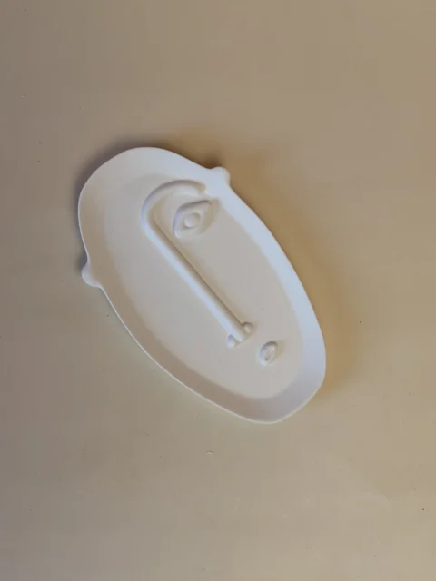Base Rosto branca e oval, com um rosto estilizado em relevo, vista de cima