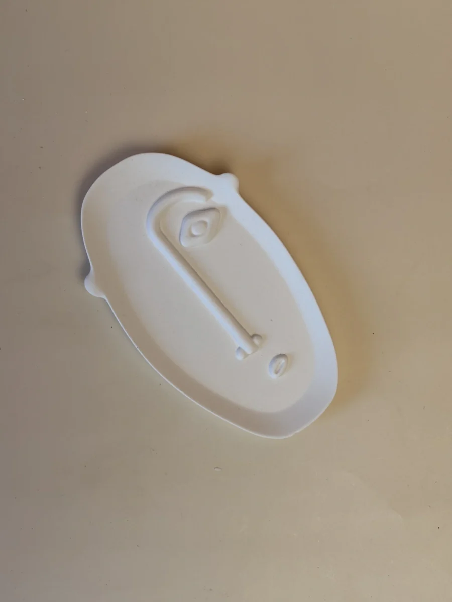 Base Rosto branca e oval, com um rosto estilizado em relevo, vista de cima