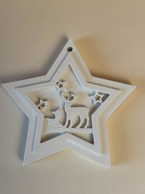 Pormenor de um pendente branco em forma de estrela, com renas e pequenas estrelas recortadas e orifício para pendurar.