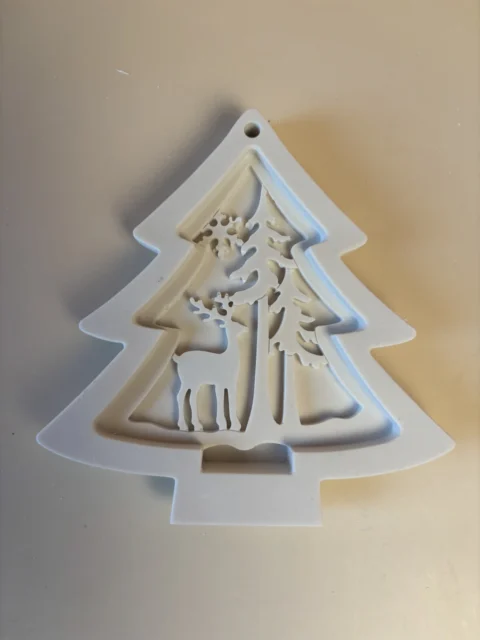 Pendente branco em forma de árvore de Natal, com rena e pinheiros recortados no interior e orifício no topo.