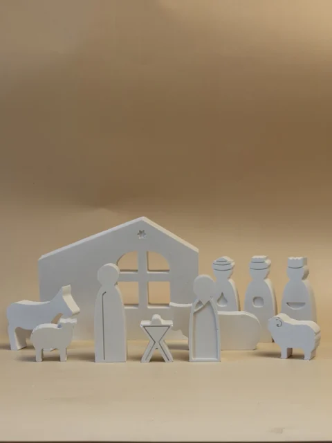 Presépio branco de figuras planas, com a Sagrada Família, Reis Magos e animais diante de uma casa, visto de frente.
