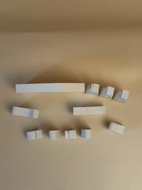 Vista de cima das peças de um presépio branco, com a casa ao fundo e as figuras e os animais alinhados à frente.