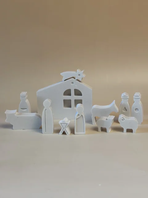 Presépio branco de figuras simplificadas, com a Sagrada Família, Reis Magos e animais diante de uma casa com estrela.