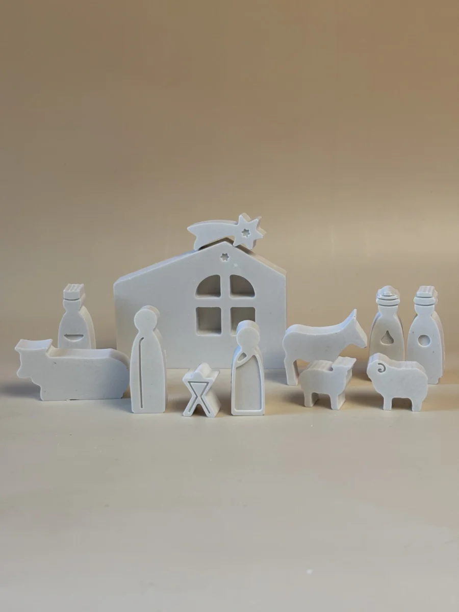 Presépio branco de figuras simplificadas, com a Sagrada Família, Reis Magos e animais diante de uma casa com estrela.