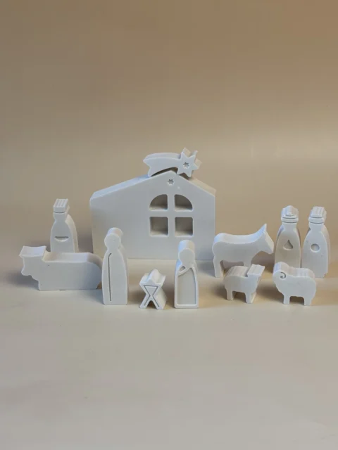 Presépio branco visto ligeiramente de lado, com a Sagrada Família, Reis Magos e animais em redor de uma casa com estrela.