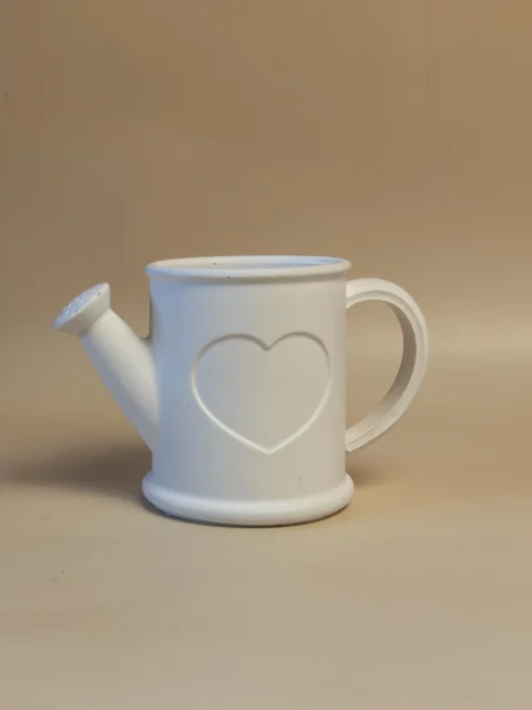 Regador decorativo branco com coração em relevo na frente, asa curva e bico inclinado.