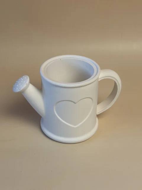 Regador decorativo branco com coração em relevo, asa lateral e bico inclinado, visto de cima e de frente.