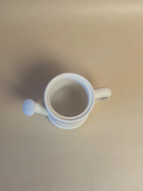 Regador decorativo branco visto de cima, com abertura circular, asa e bico com pequenos orifícios.